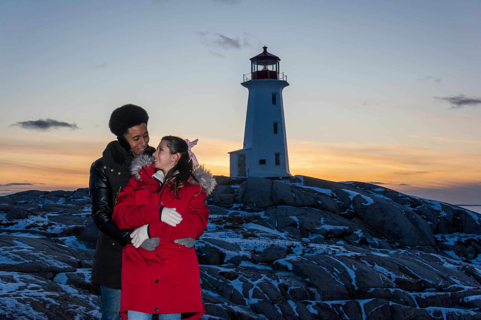 During the winter a couple pose in front of the lighthouse at Peggy's Cove, Nova Scotia - image by Picture Perfect Tours and Geordie Mott