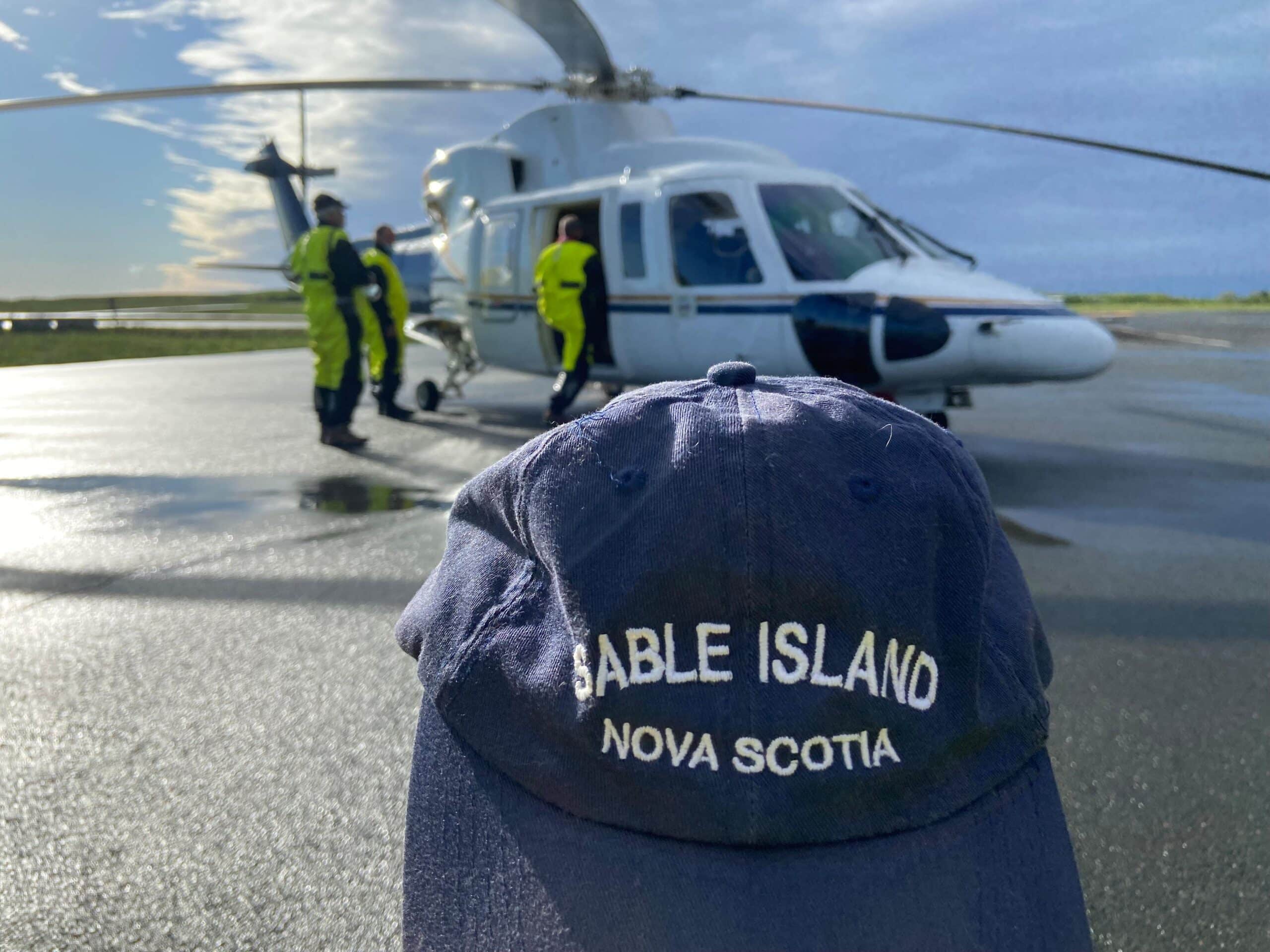 Helicopter ride to sable island. A photo of a baseball-style hat with the words Sable Island Nova Scotia on it in front of a helicopter that had recently landed on the island